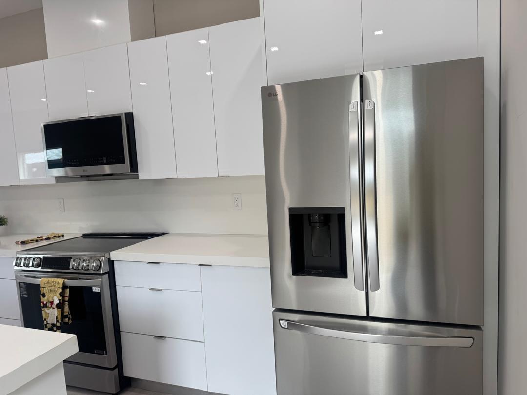 Remodeled kitchen with high-gloss white cabinetry and stainless steel refrigerator